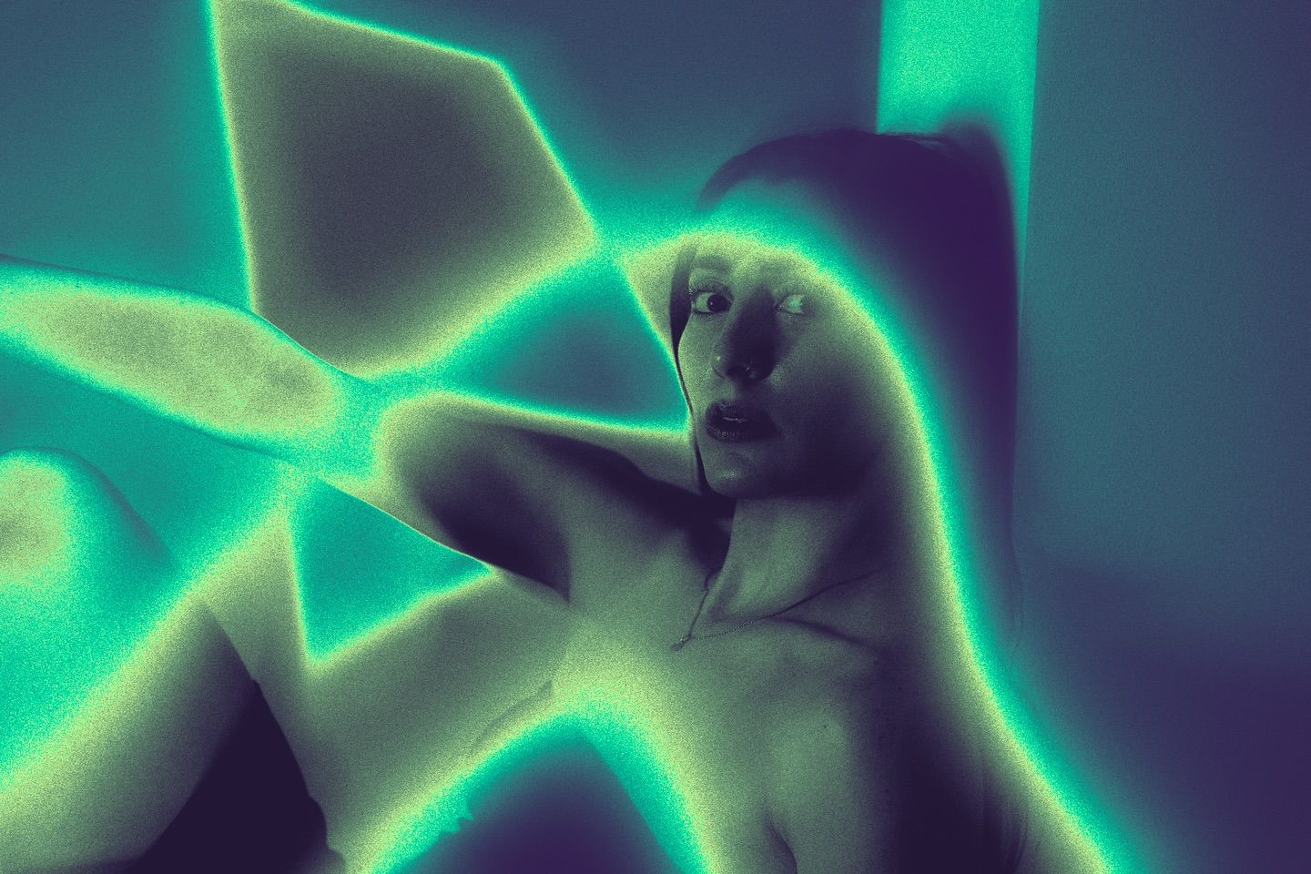 A woman crouches low, lit by jagged turquoise light shapes that cross her face and body against a dark background.